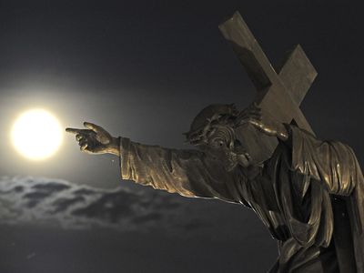 A statue in front of the Holy Cross church in Warsaw, Poland, guides viewers toward the August 2014 supermoon.