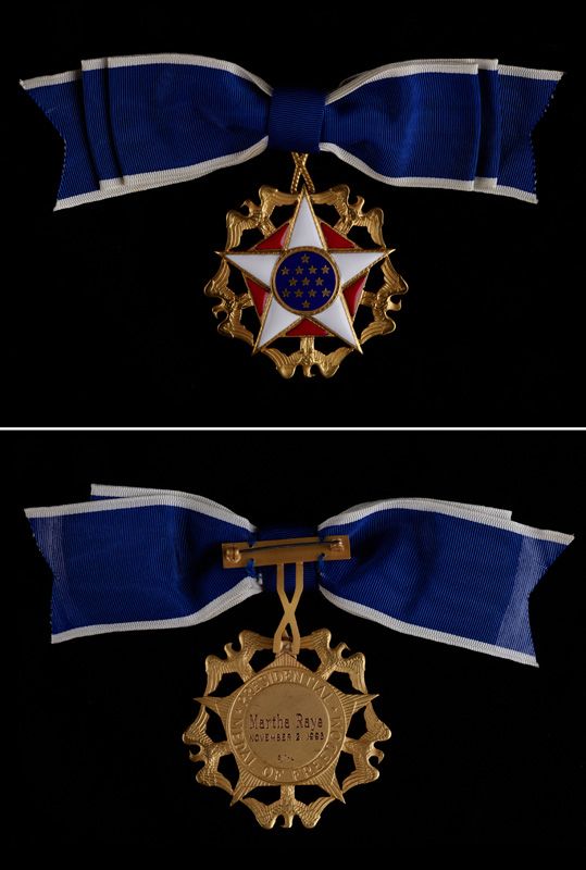 Front and back of Martha Raye's Presidential Medal of Freedom. The medal hangs on a blue ribbon. The medal's front is decorated with stars and golden eagles; its back includes the inscription, Martha Raye, November 2, 1993.