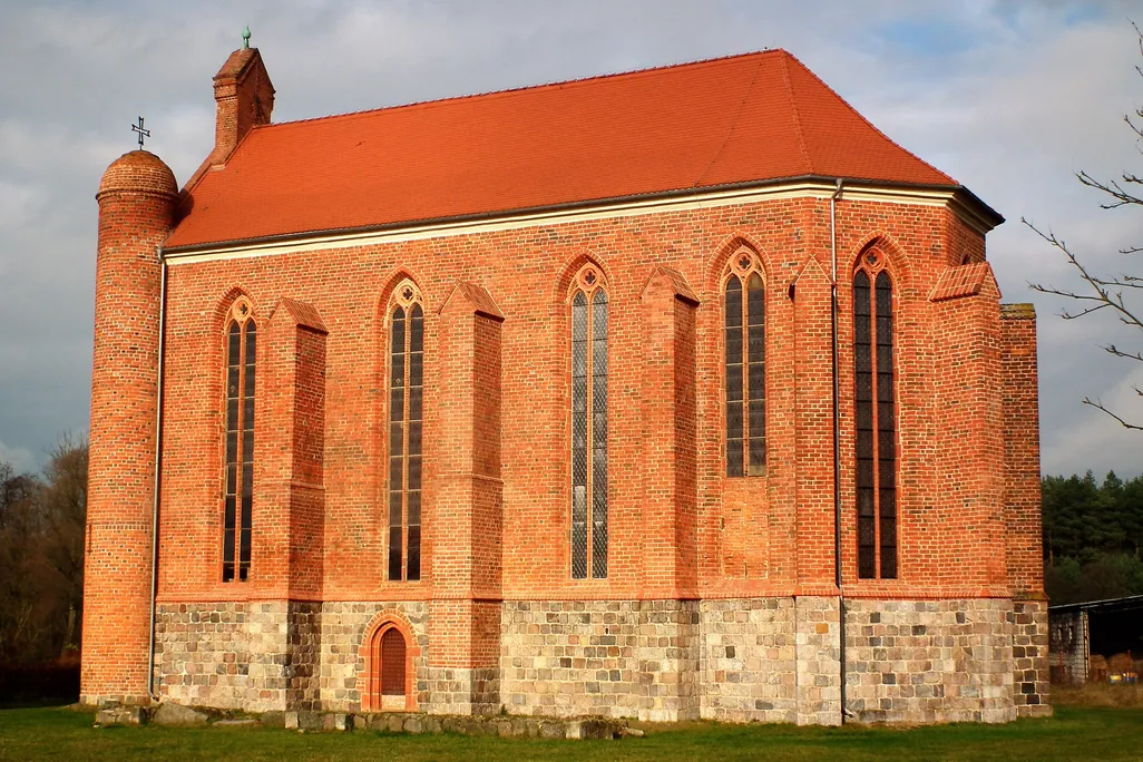 The exterior of an orange brick chapel with skinny, tall Gothic windows, a gabled red roof and a curved nave on one end.
