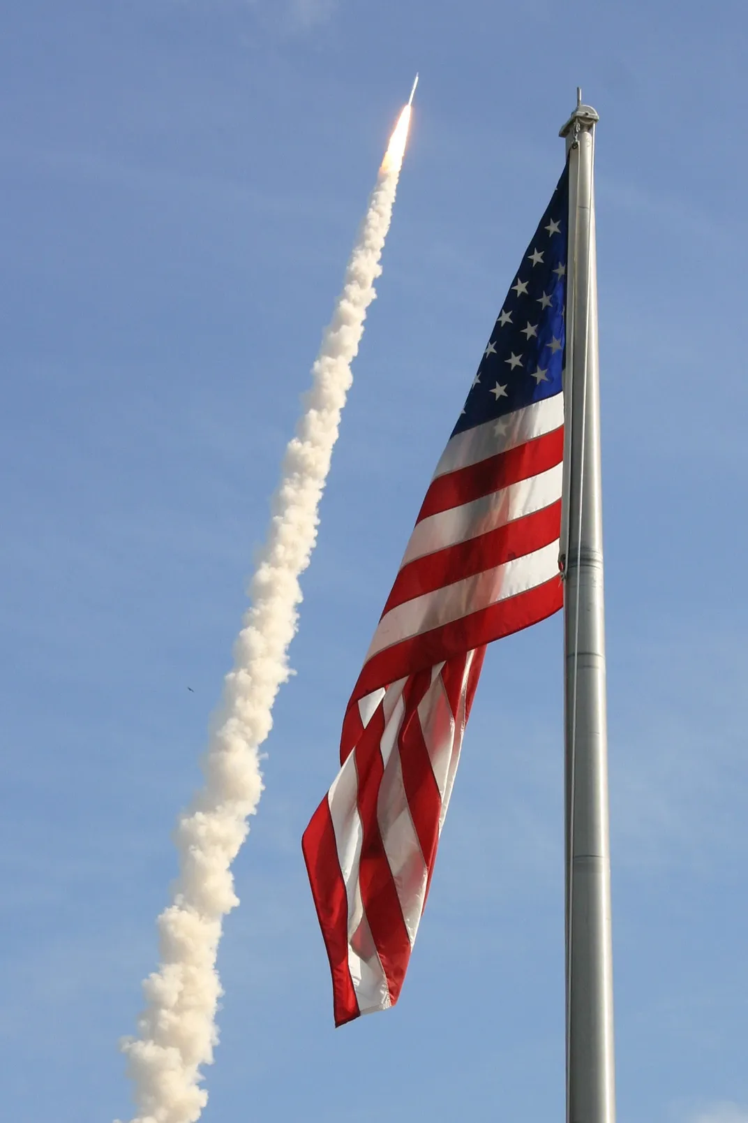 12 - A United States flag gently wafts in the air in the foreground as the Ares I-X rocket takes flight.