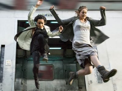 The protagonist, Tris (Shailene Woodley), and her friend Christina (Zoë Kravitz) jump from a train running through post-apocalyptic Chicago in a scene from the film Divergent. 