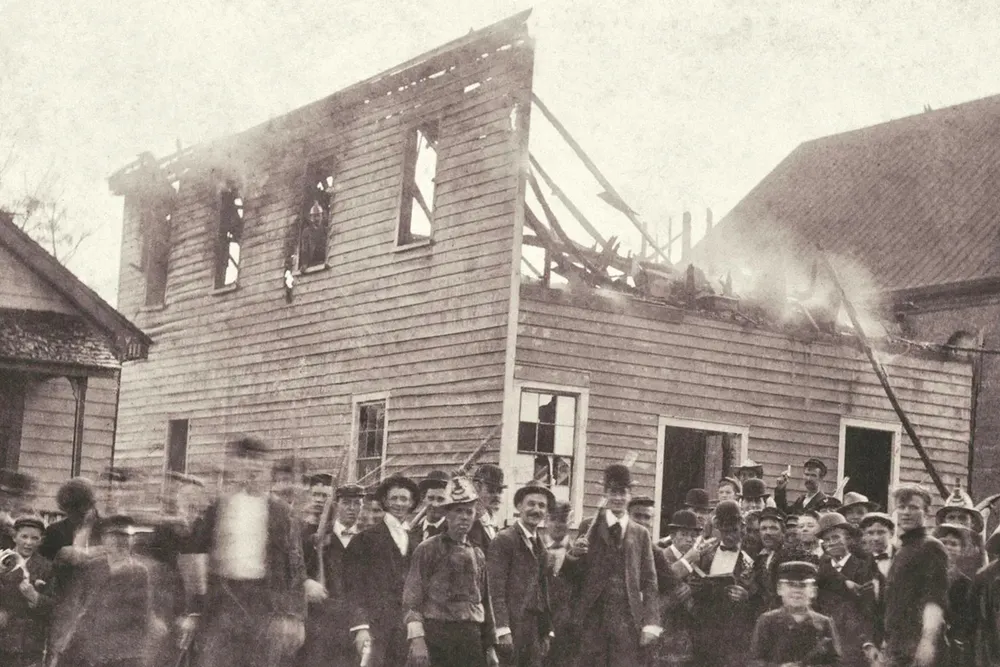 A white mob poses outside of the razed office of the Daily Record, a Black-owned newspaper in Wilmington, North Carolina.