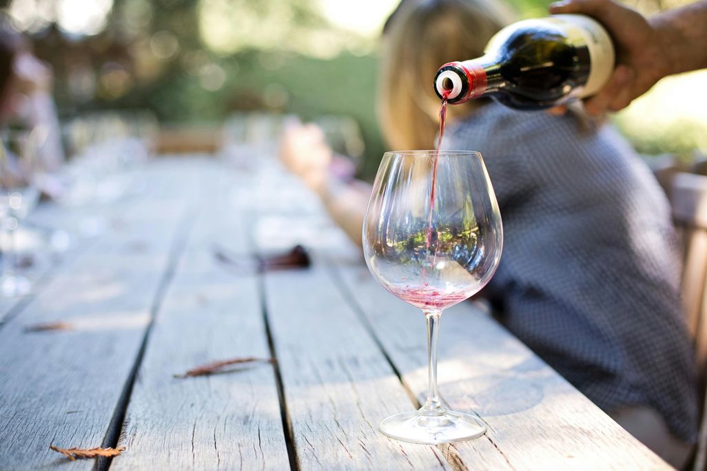 Hand pouring a glass of wine from a bottle on a wooden table