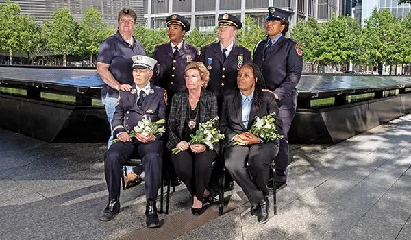 seven women first responders looking solemn, most in uniform, at the Ground Zero Memorial