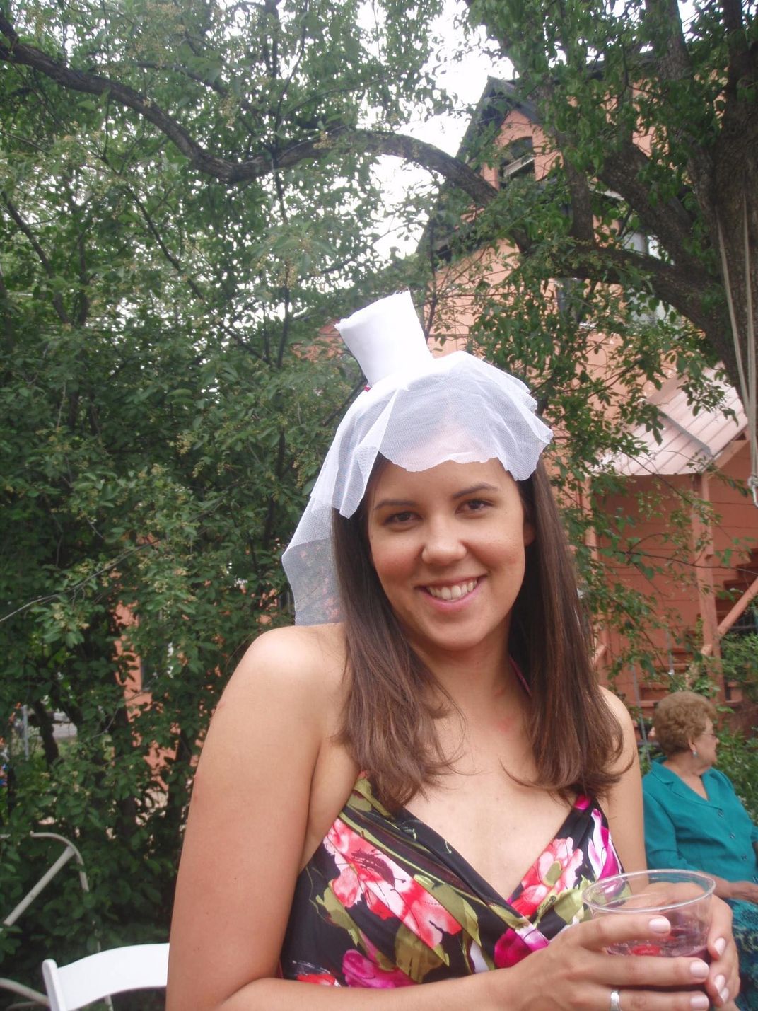 Photo of woman wearing a pink floral top, smiling with a white cup on her head