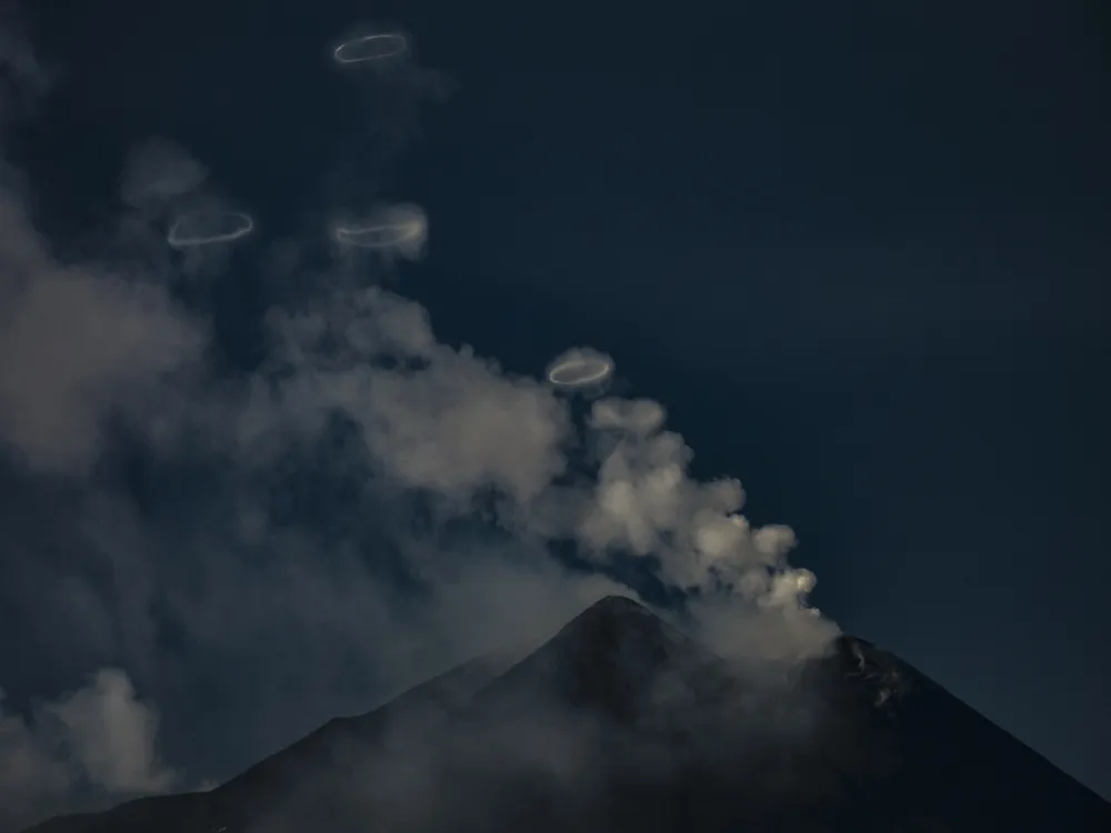 A volcano with wisps of clouds and rings floating above
