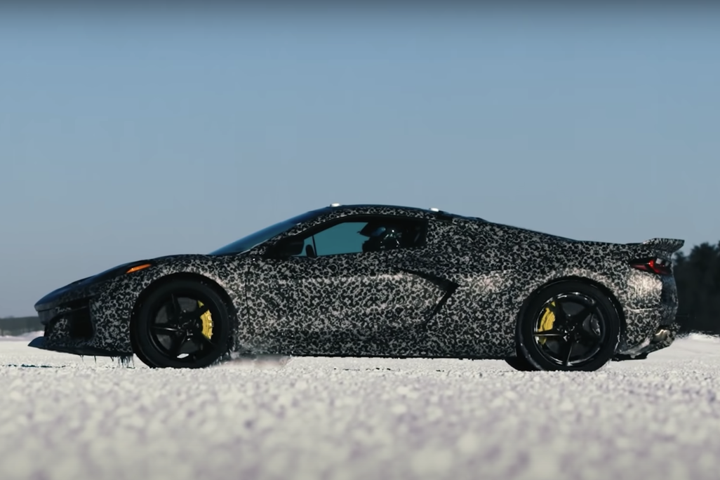 An image of a Corvette with a camouflage wrap sitting idle in snow. The car also has yellow calipers by near its black rimmed wheels.