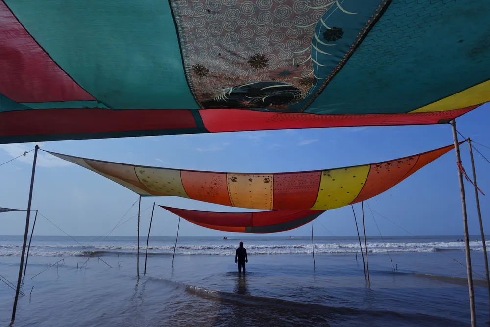 The beach becomes a canvas of colors, where traditional fabrics dance above the waves and the sea reflects stories stitched into every fold.