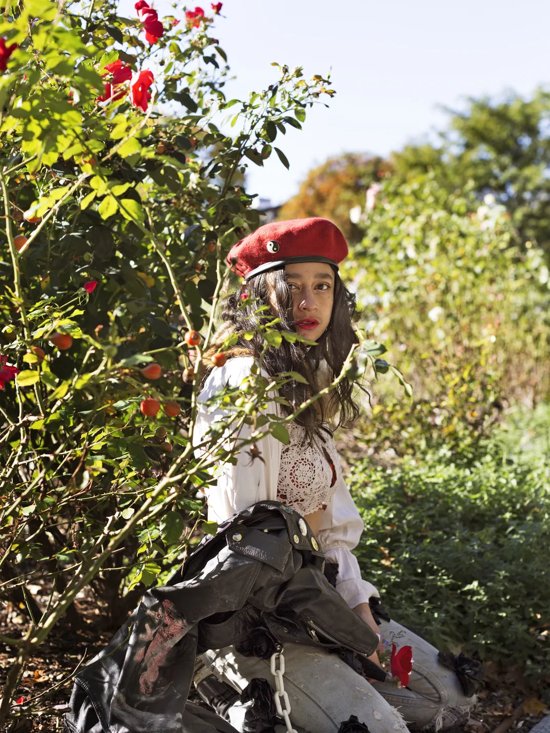 A woman with brown hair and a red beret poses next to a lush green plant with red flowers