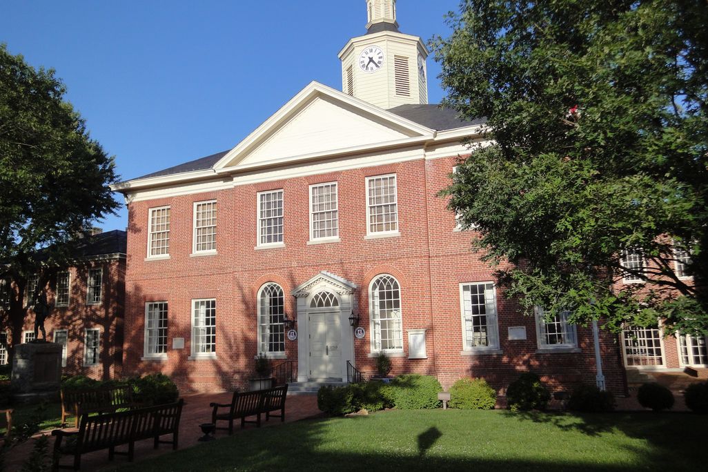 A red brick old-fashioned courthouse in front of a blue sky and a manicured green lawn
