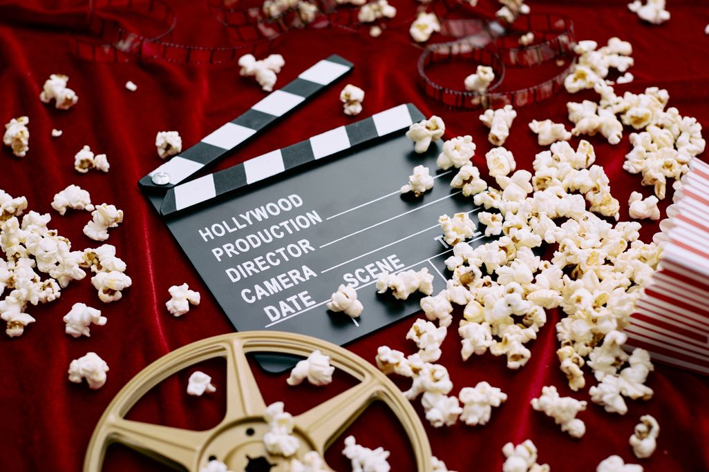 Clapperboard, film reel, film and spilled popcorn on red satin background.