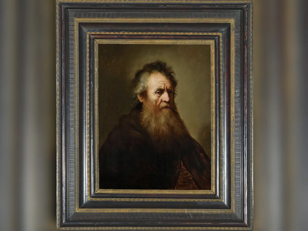 Un portrait dans un cadre doré d'un homme âgé avec une barbe hirsute, des cheveux grisonnants et portant un simple vêtement sombre