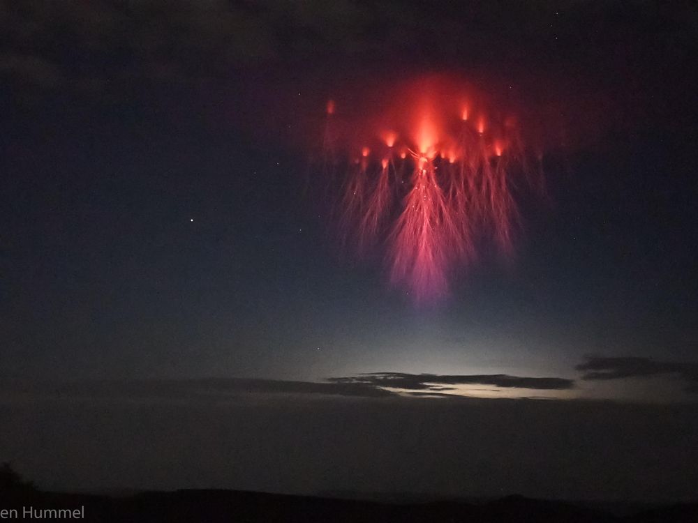 A red cloud of light hangs in the clouds with tentacles of red lightning dangling below.