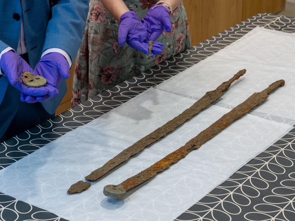 Pair of gloved hands next to long skinny swords