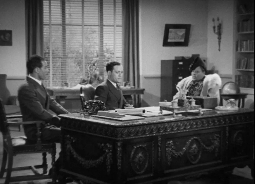 Black and white image showing three people sitting around a desk