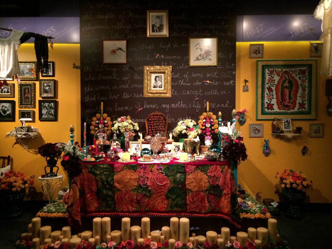 Elaborate and colorful altar built on a bedpost, with photos, food, dozens of candles, marigolds and roses, and other handmade details