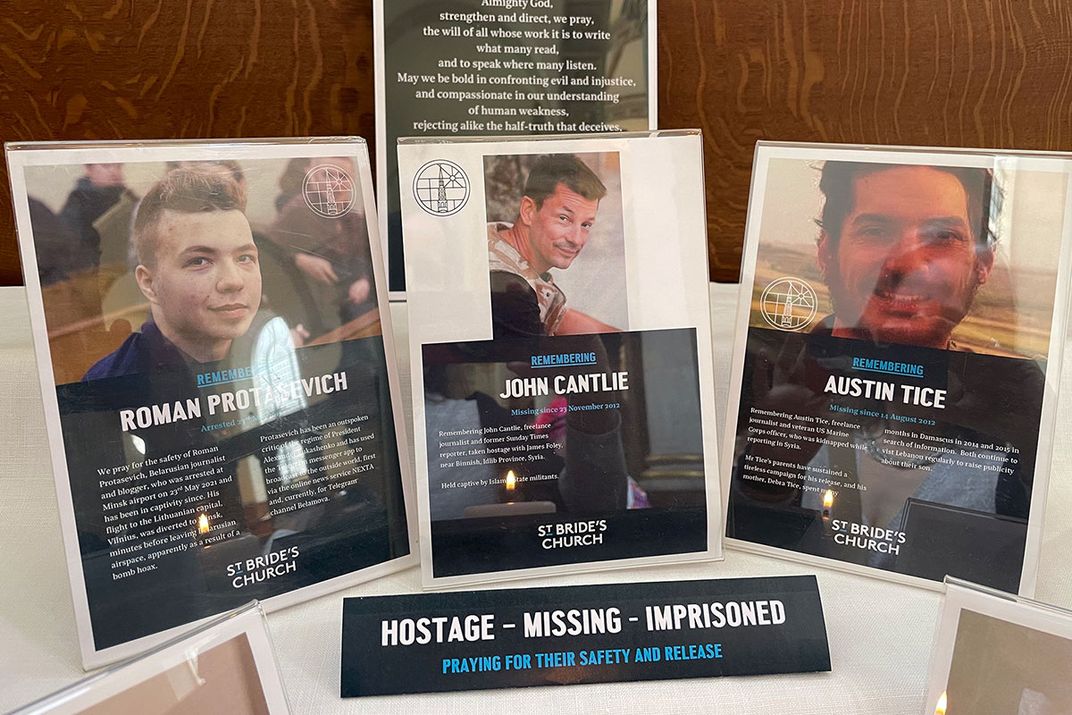 Close-up on three of the memorial cards on the altar, from Roman Protasevich, John Cantlie, and Austin Tice. A small text card in front of them reads, Hostage - Missing - Imprisoned. Praying for their safety and release.