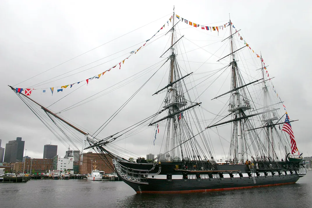 A large painted wooden ship decorated with flags in a city harbor