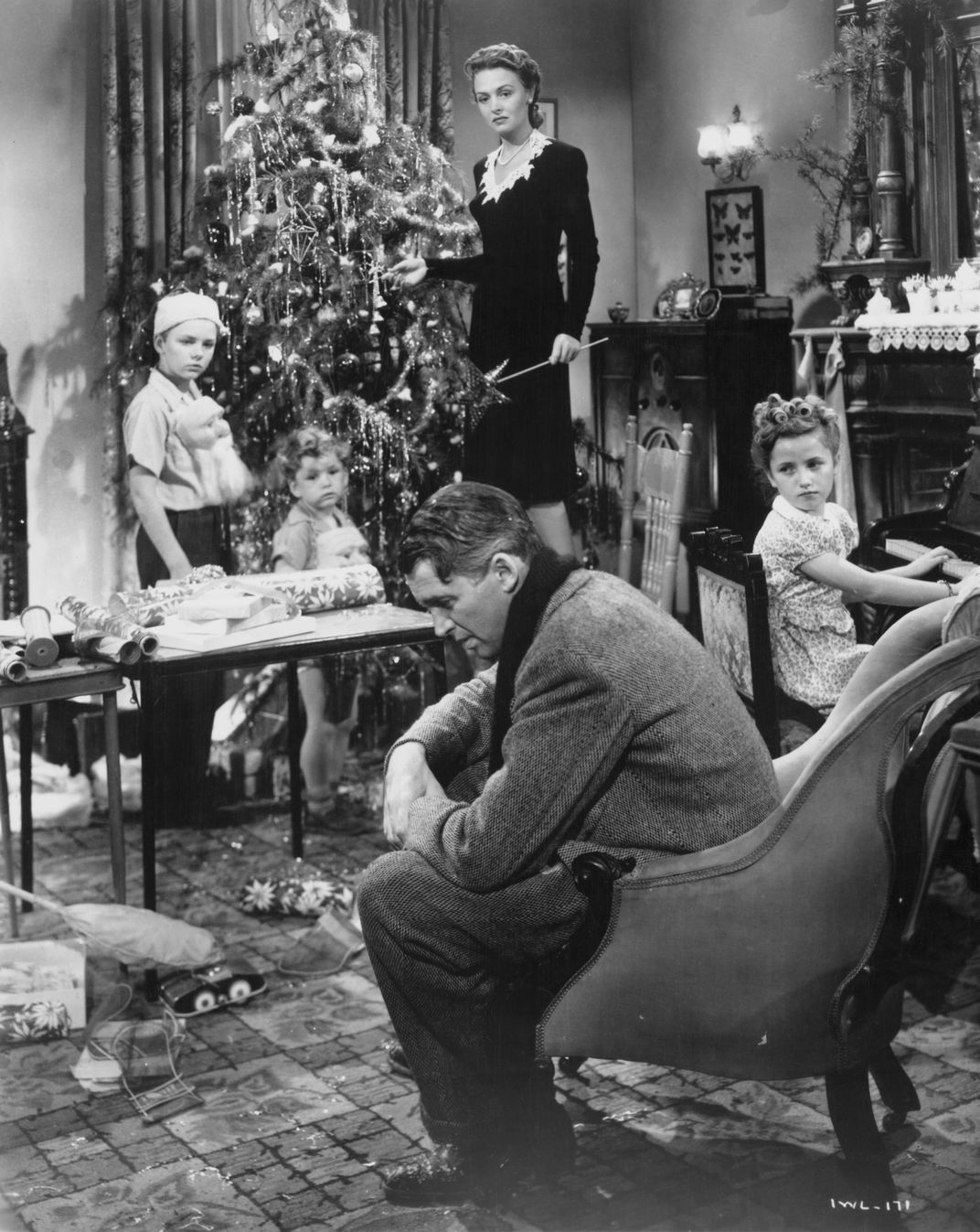 George Bailey sits in a chair in his living room, surrounded by his wife and children
