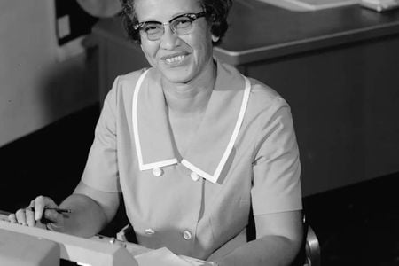 A black and white photo of Katherine Johnson sitting at a desk in front of a typewriter and open notebook.