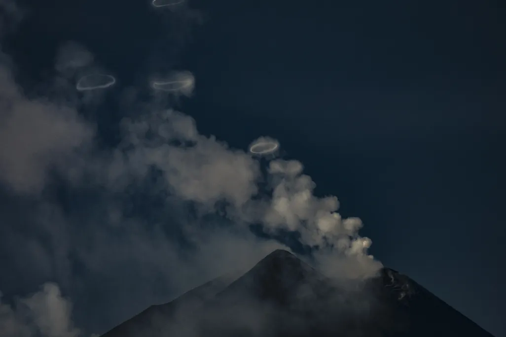 A volcano with wisps of clouds and rings floating above