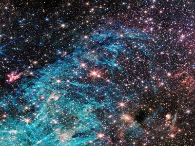 A multitude of stars packed together in a dense region of space, shining brightly in the surrounding darkness. A bright blue cloud in the lower half of the image with pitch black patches appearing within the cloud