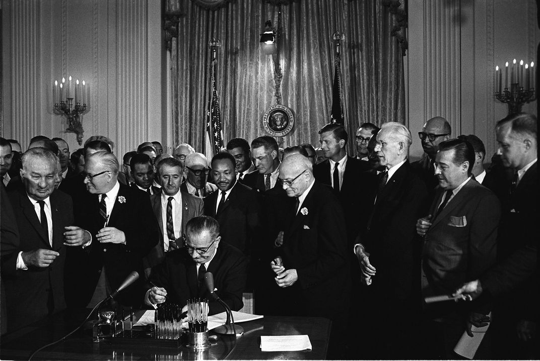 Johnson signs the Civil Rights Act of 1964 as Martin Luther King Jr. looks on.
