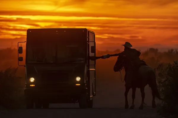 A cowboy accepts a package from a delivery driver on an Arizona ranch at sunset thumbnail