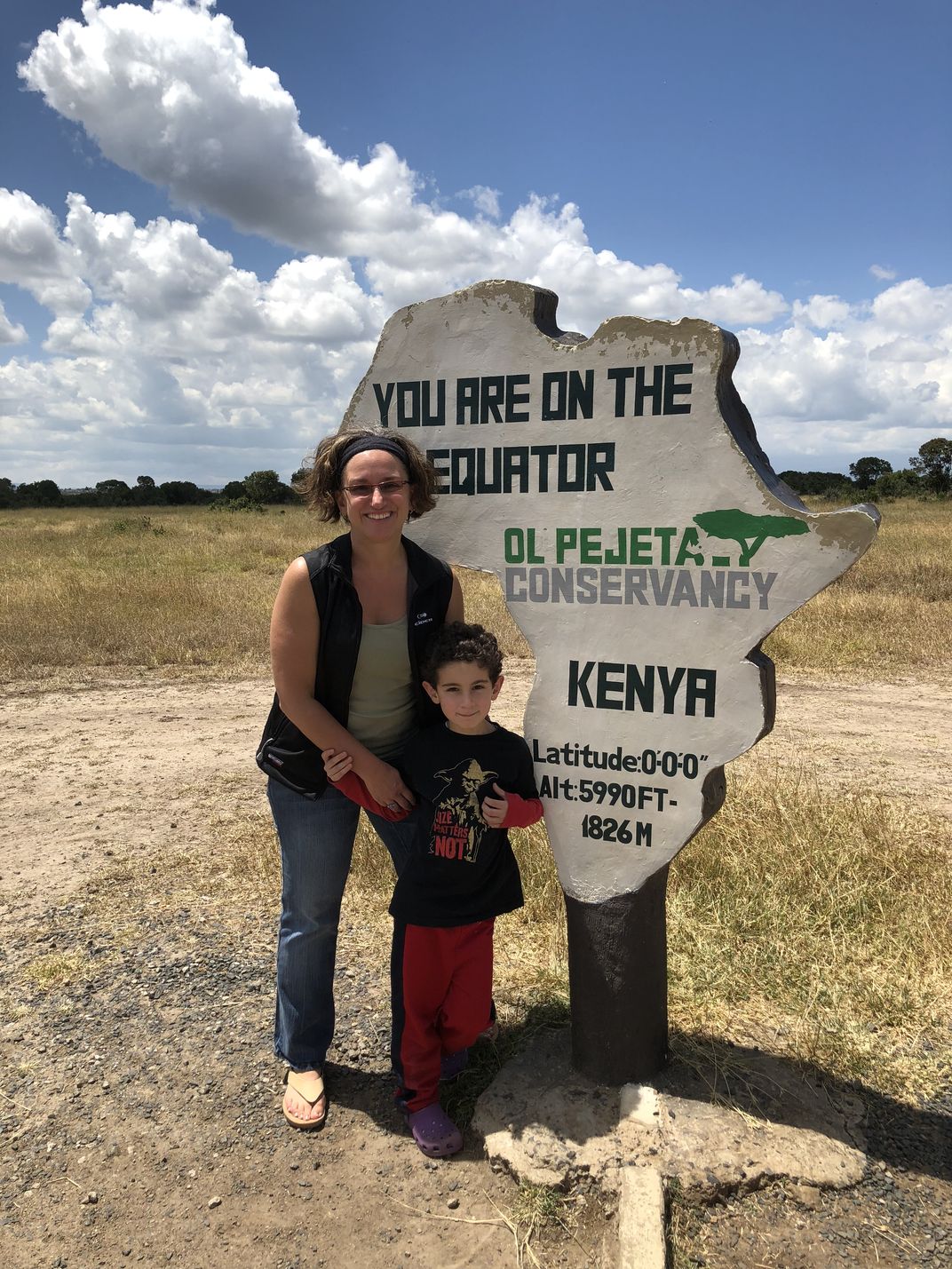 A young boy and adult woman next to a white sign marking the equator in Kenya.