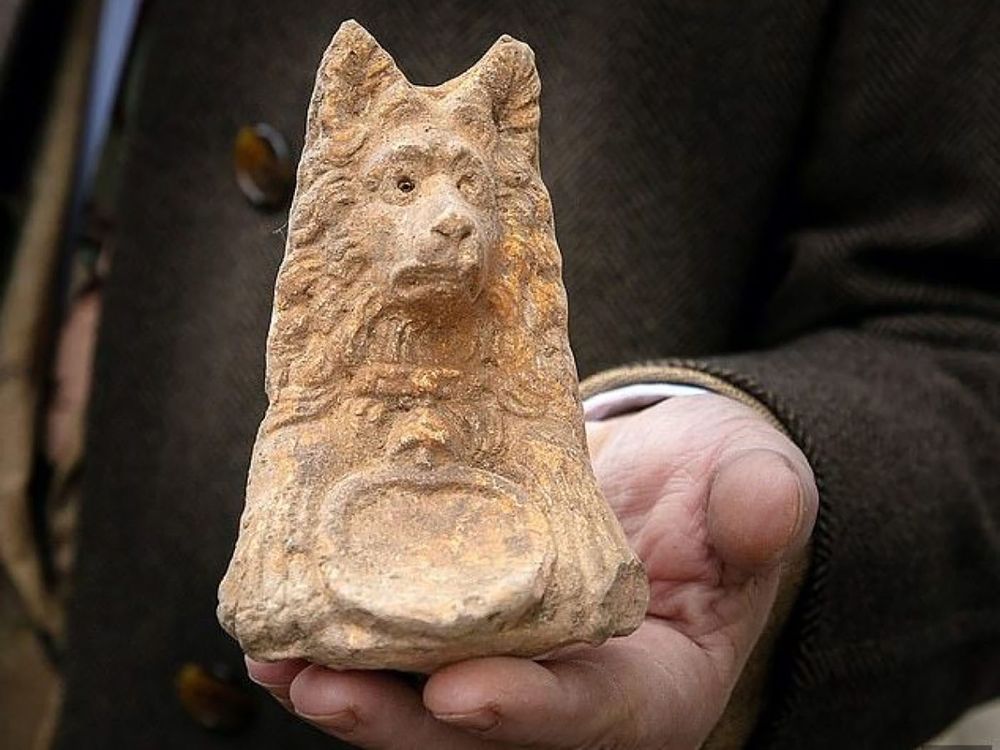 clay figure of dog with pointy ears, color with large emblem and long shaggy fur