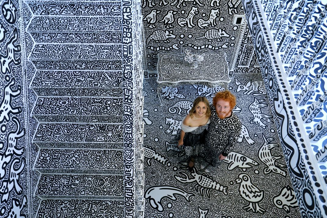 Artist Sam Cox and his wife, Alena, standing in their scrawled mansion.