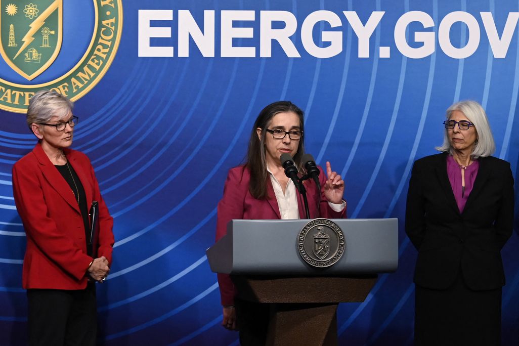 three women at a podium in front of a wall that reads energy.gov