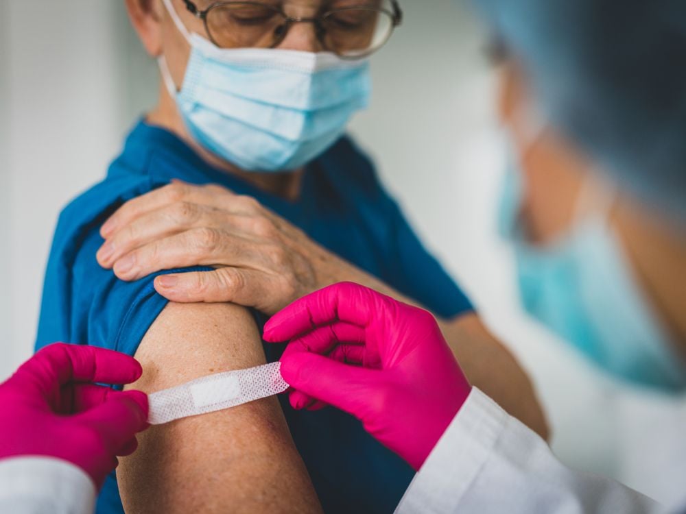 A doctor with pink gloves applies a bandaid to an older woman's arm