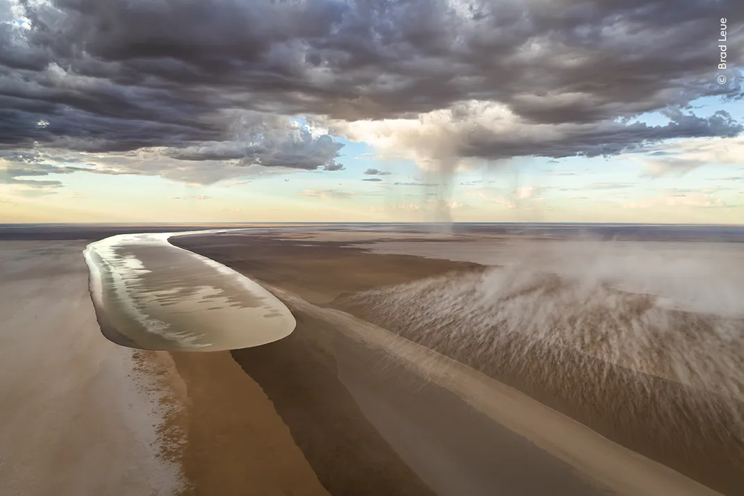 floodwaters advance across a desert landscape as clouds and rains surround it
