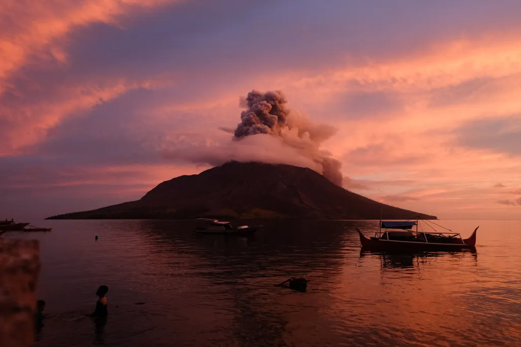 a volcano on an island spewing ash at sunrise