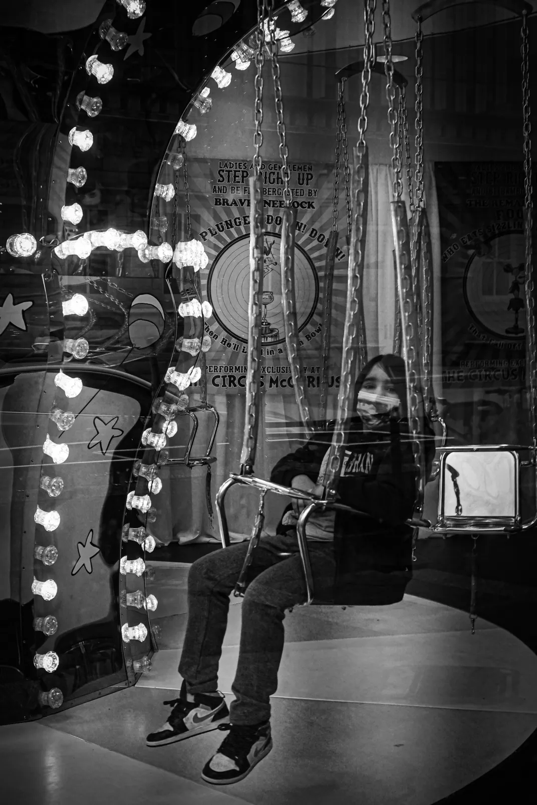 A child sits with a mask on a swig ride in a black and white photo
