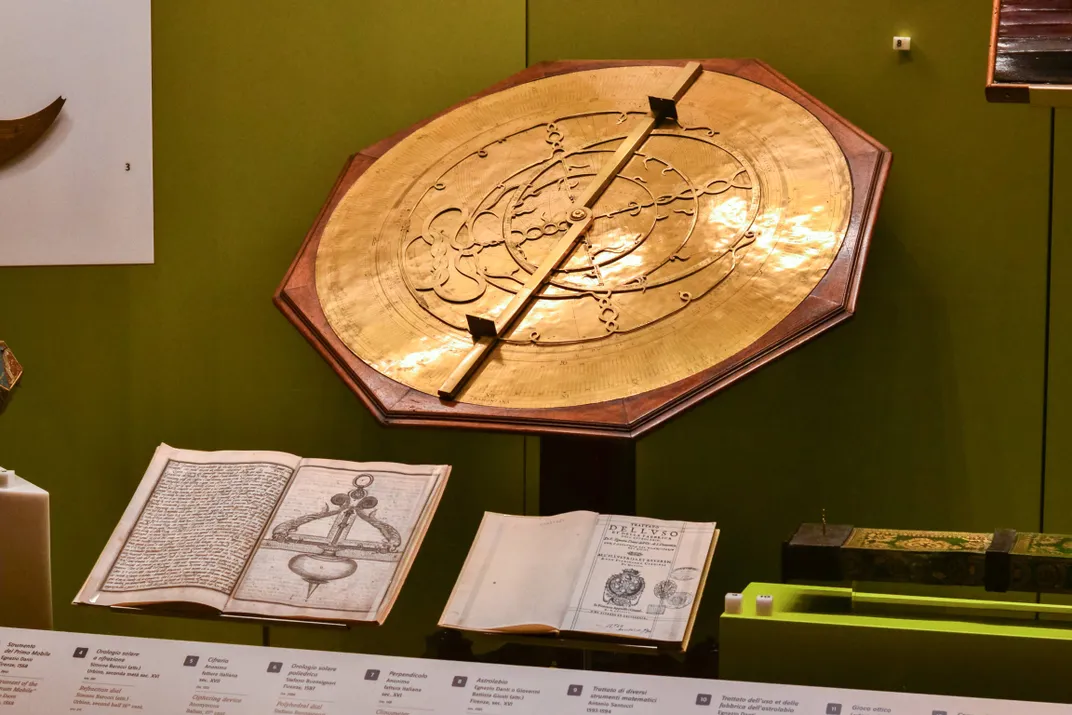 in a museum display case, a golden astrolabe sits on a tilted table