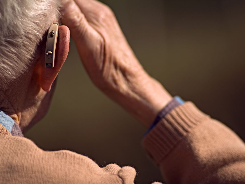 A person wearing a hearing aid, seen from the back, touches their head