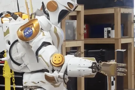 A NASA Valkyrie robot picks up an item with its hand.