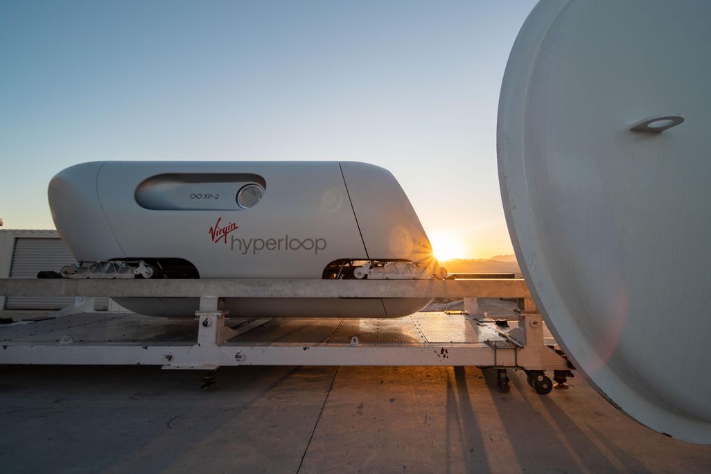 The image shows a white transportaion vehicle on a track with the sun setting behind it. 
