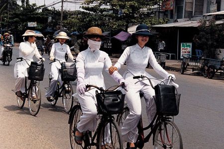 Ao dais make striking uniforms for four university students heading home after classes. Long gloves and hats provide welcome protection from the sun in a land where a suntan is not considered fashionable; masks serve as barriers to dust and exhaust.