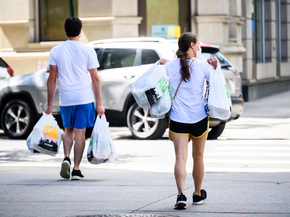 Two people walk down street carrying groceries in plastic bags in New York