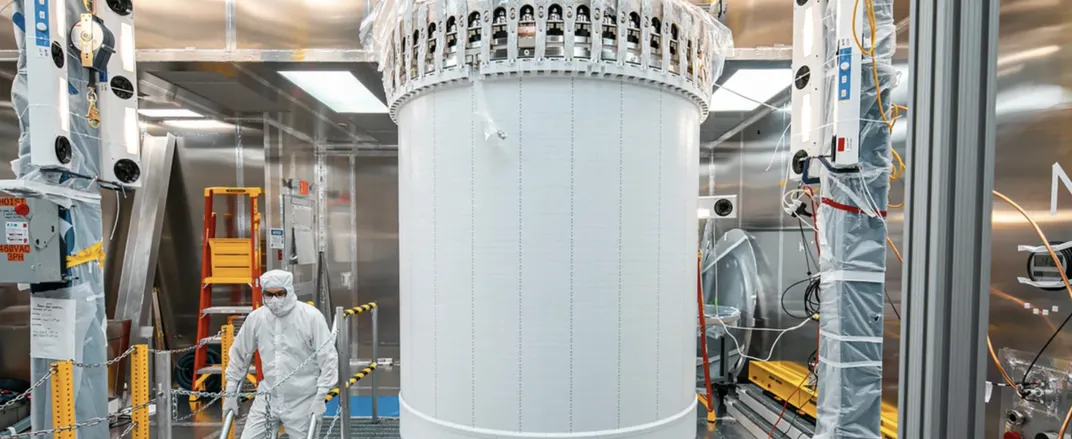 a person in a hazmat suit next to a vertical white tube looking thing
