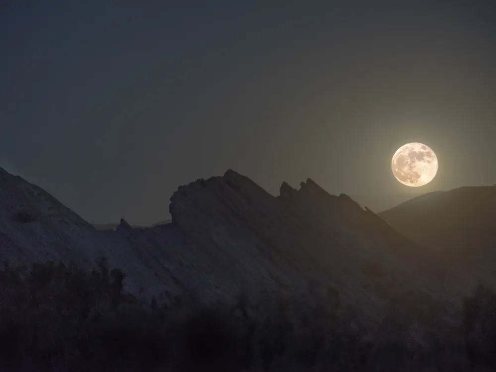 full moon glowing above rocky highlands in the foreground