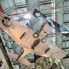 A World War II military airplane is photographed from below while hanging from the ceiling. The underside of the airplane is painted white and the wing and forward fuselage are wrapped in opaque plastic.