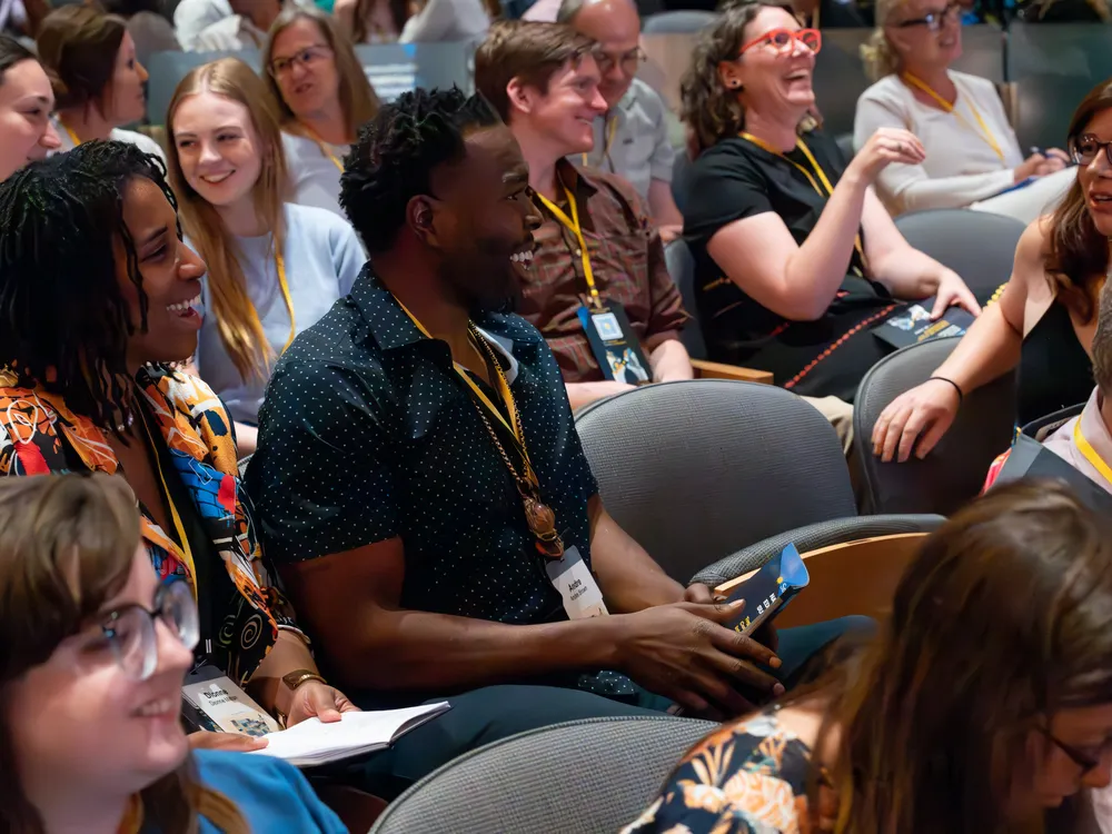 A group of men and women are in an audience turning and talking to each other with smiles