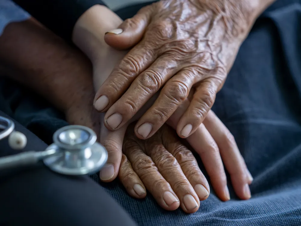 A close-up of a young nurse holding the wrinkled hands of an older person.