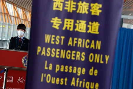 A quarantine official at Beijing's international airport stands behind a banner notifying incoming passengers from West Africa'  to use a specific lane  