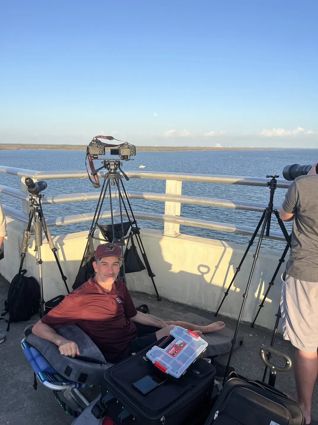 a man sits in a folding chair on a bridge behind cameras on tripods