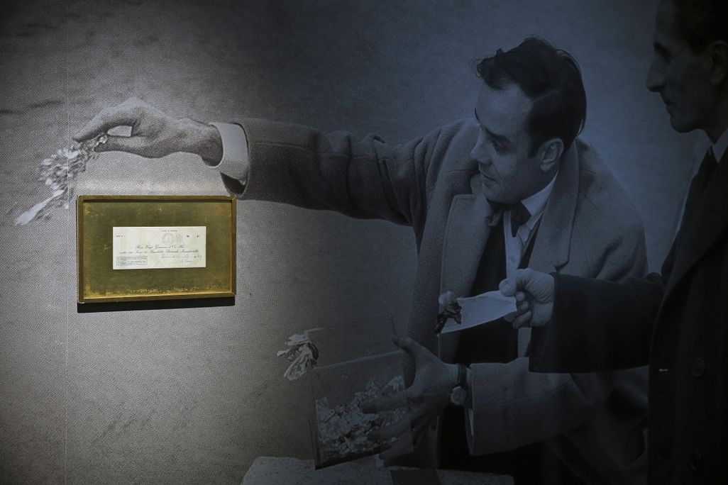 A receipt for one of Yves Klein's conceptual art pieces hangs on a wall atop a photo of the artist throwing gold into the Seine